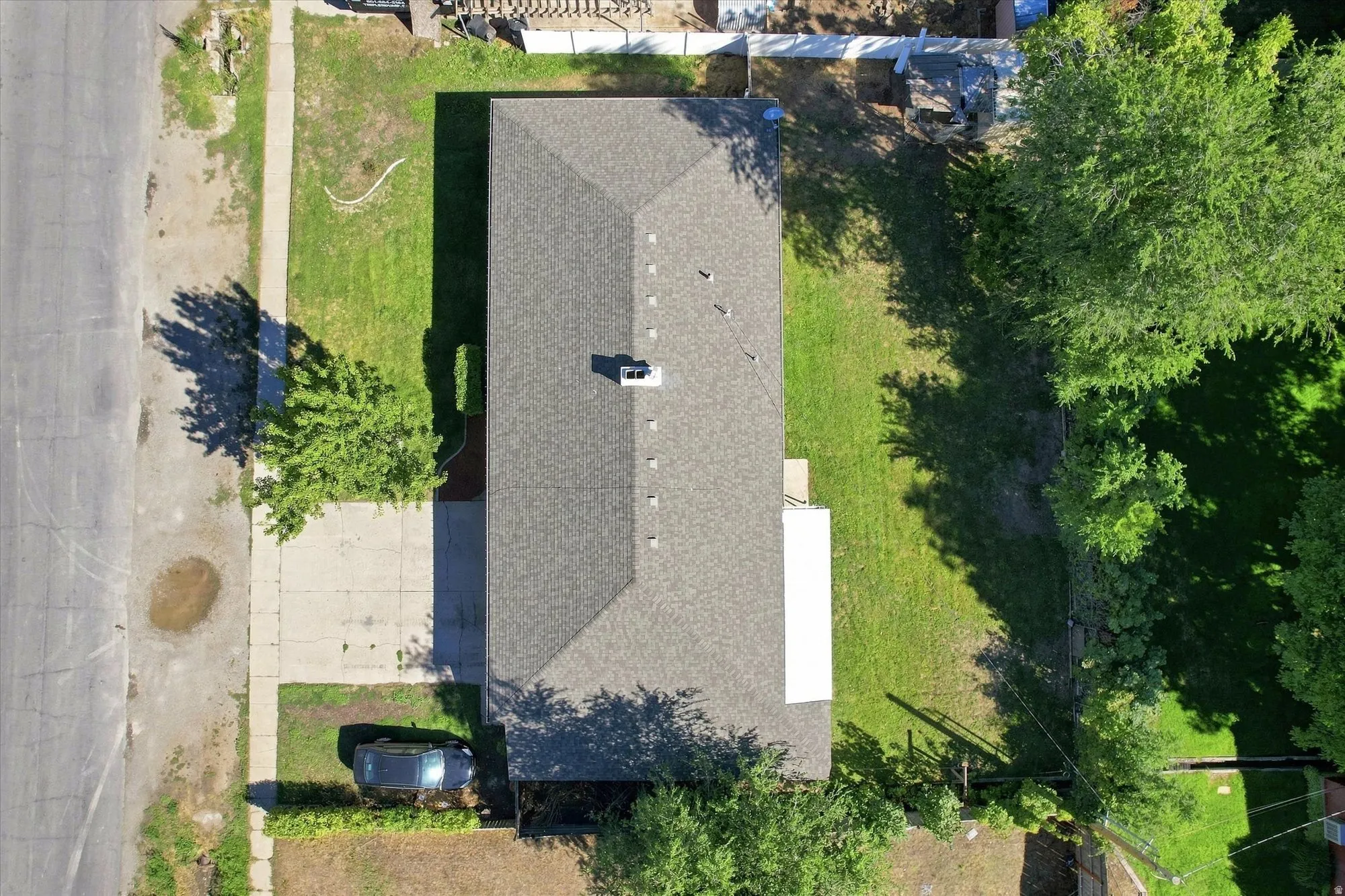 Gable roof with asphalt shingles, mature trees, green lawn, and a concrete driveway