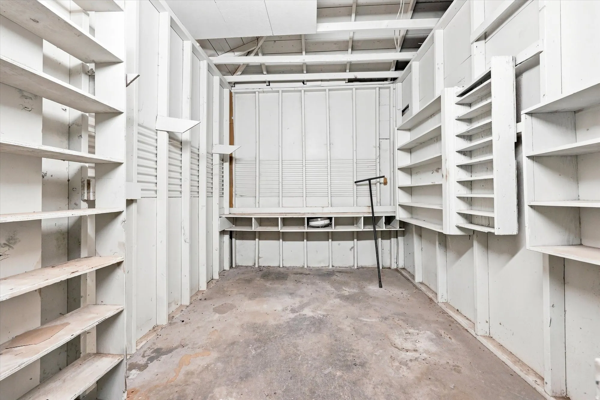 Extensive built-in shelving, concrete flooring, exposed ceiling joists, and a horizontal slatted wall panel