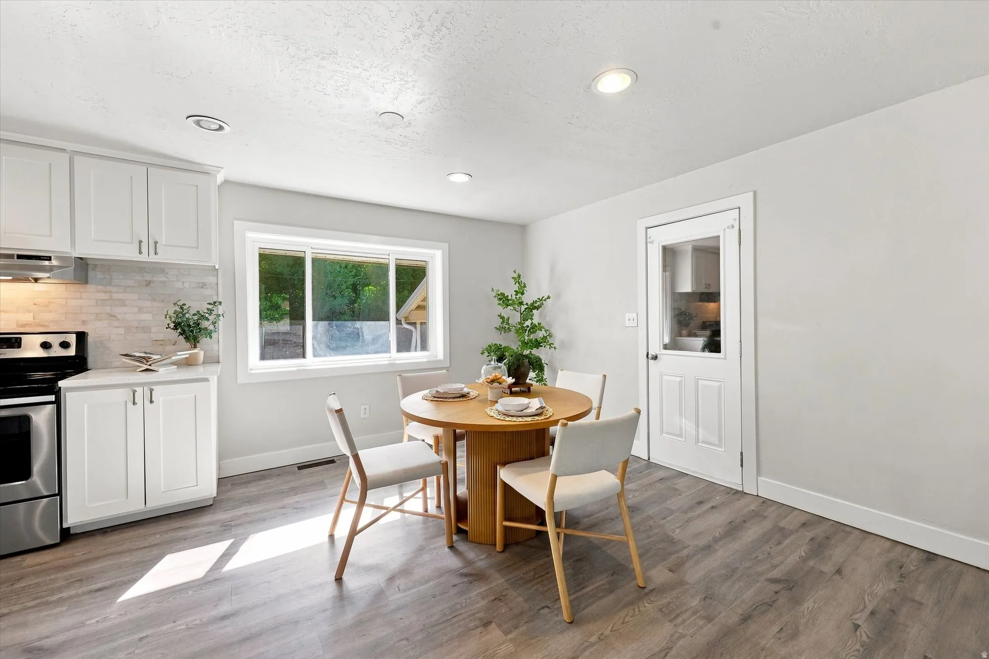 White shaker-style cabinetry, stainless steel range and hood, light-toned wood-finish flooring, recessed ceiling lighting, and a paneled door with a frosted glass insert