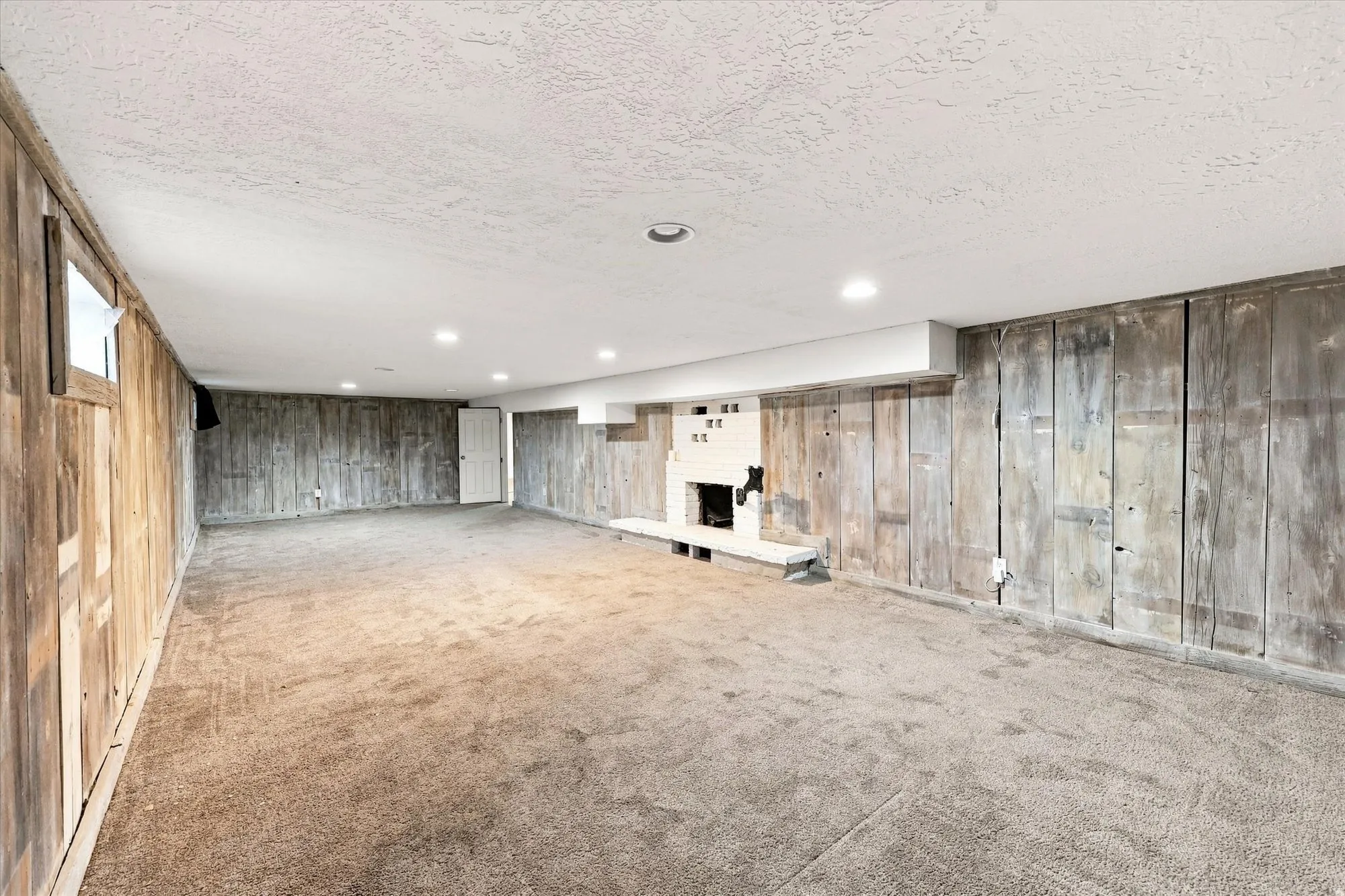 Spacious room featuring wood-panel walls, recessed lighting, and a white brick fireplace