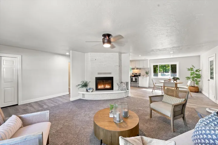 Living area featuring a white brick fireplace with an integrated hearth, a ceiling fan, and mixed flooring with carpet and wood-finish planks