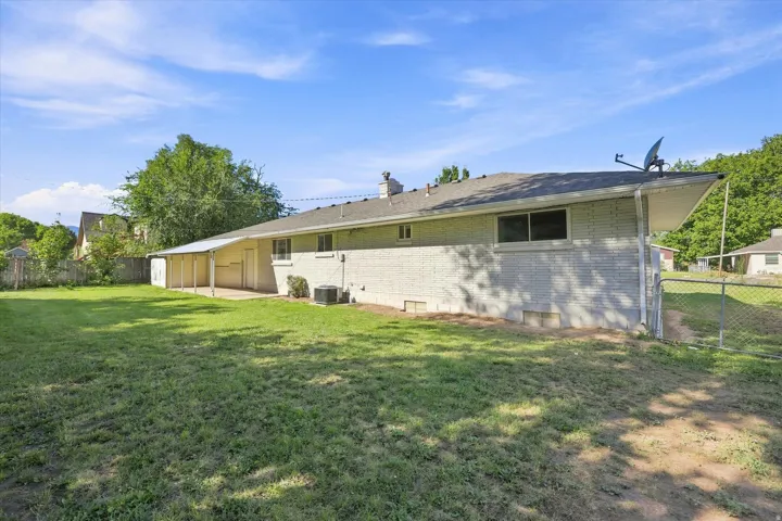 Expansive backyard featuring a manicured lawn, a covered patio, and a chain-link fence