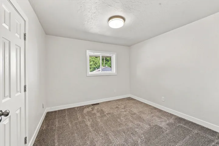 Neutral-toned carpeting, white walls, and a single window with white trim