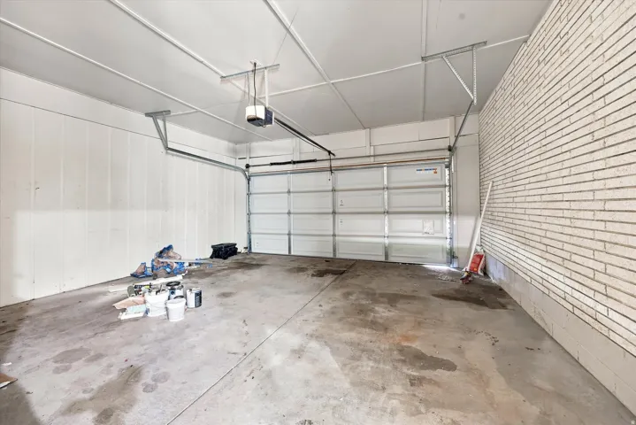 Two-car garage featuring a sectional overhead door, exposed ceiling joists, and a brick accent wall