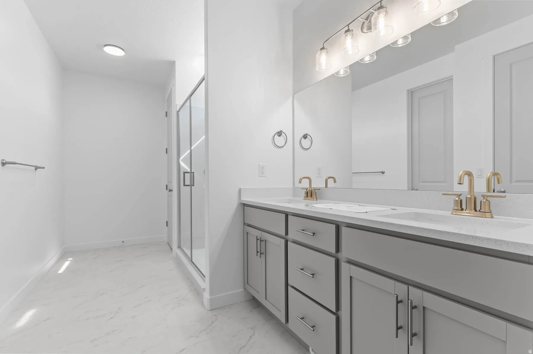 Dual vanity with light gray cabinetry, light countertops, and gold-toned faucets