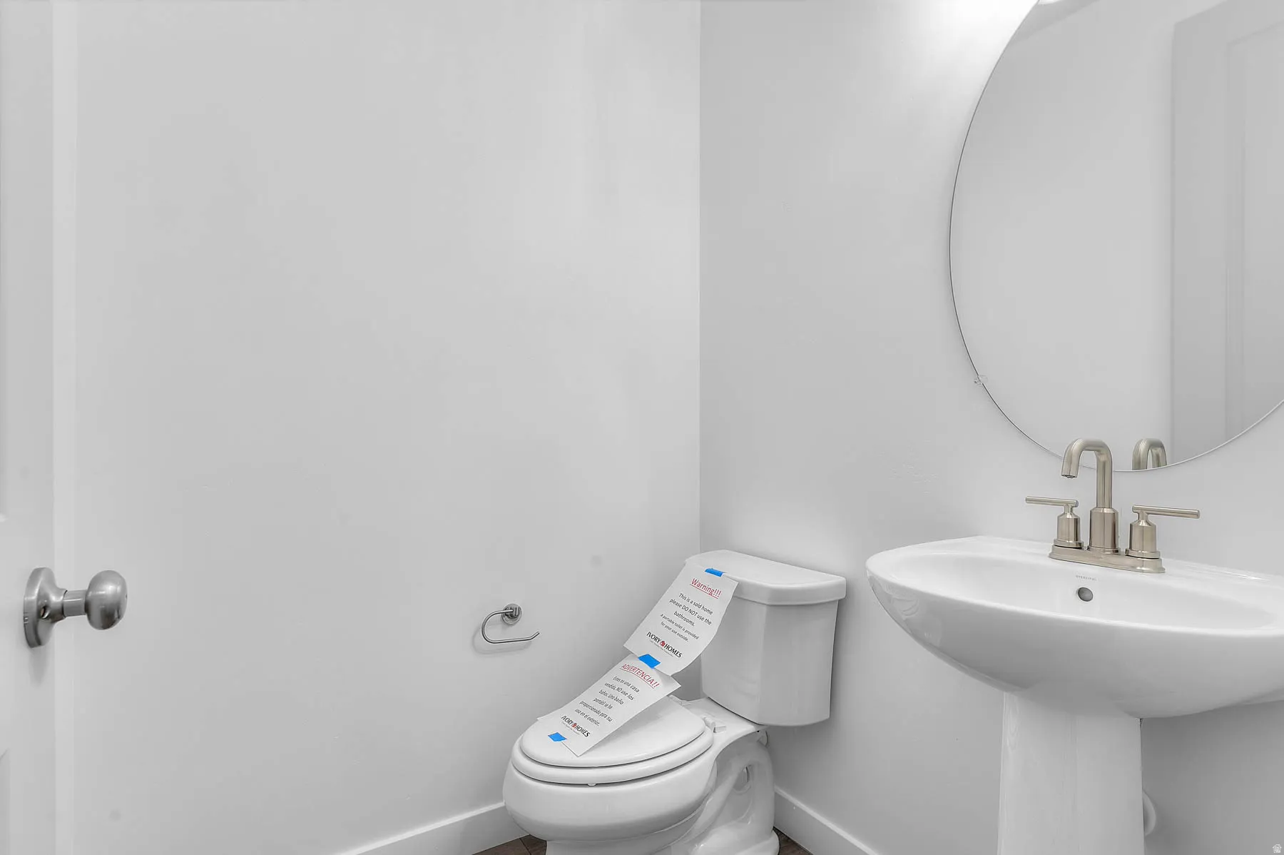 Pedestal sink with a round mirror, brushed nickel faucet, and a toilet