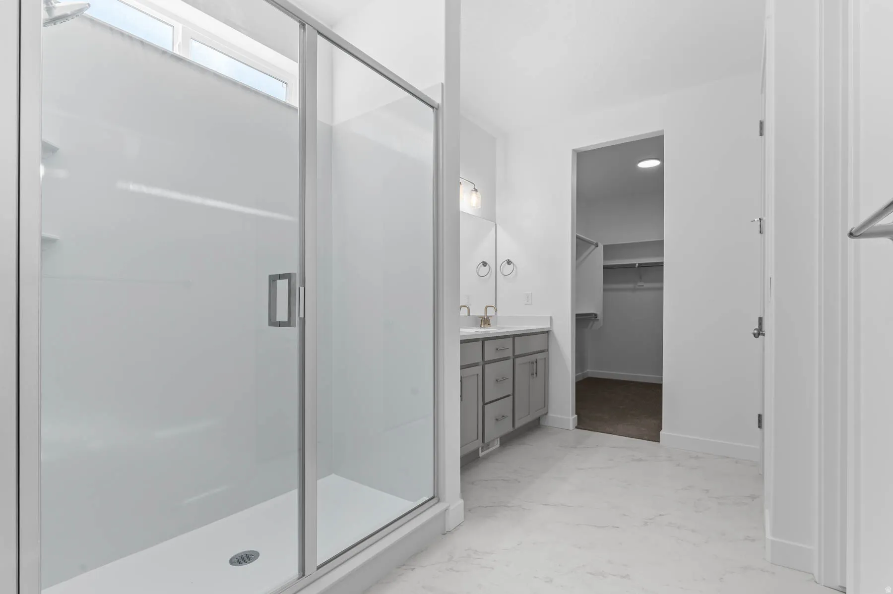 Glass-enclosed shower with a transom window, dual vanity with undermount sinks, gray cabinetry, and light-toned flooring