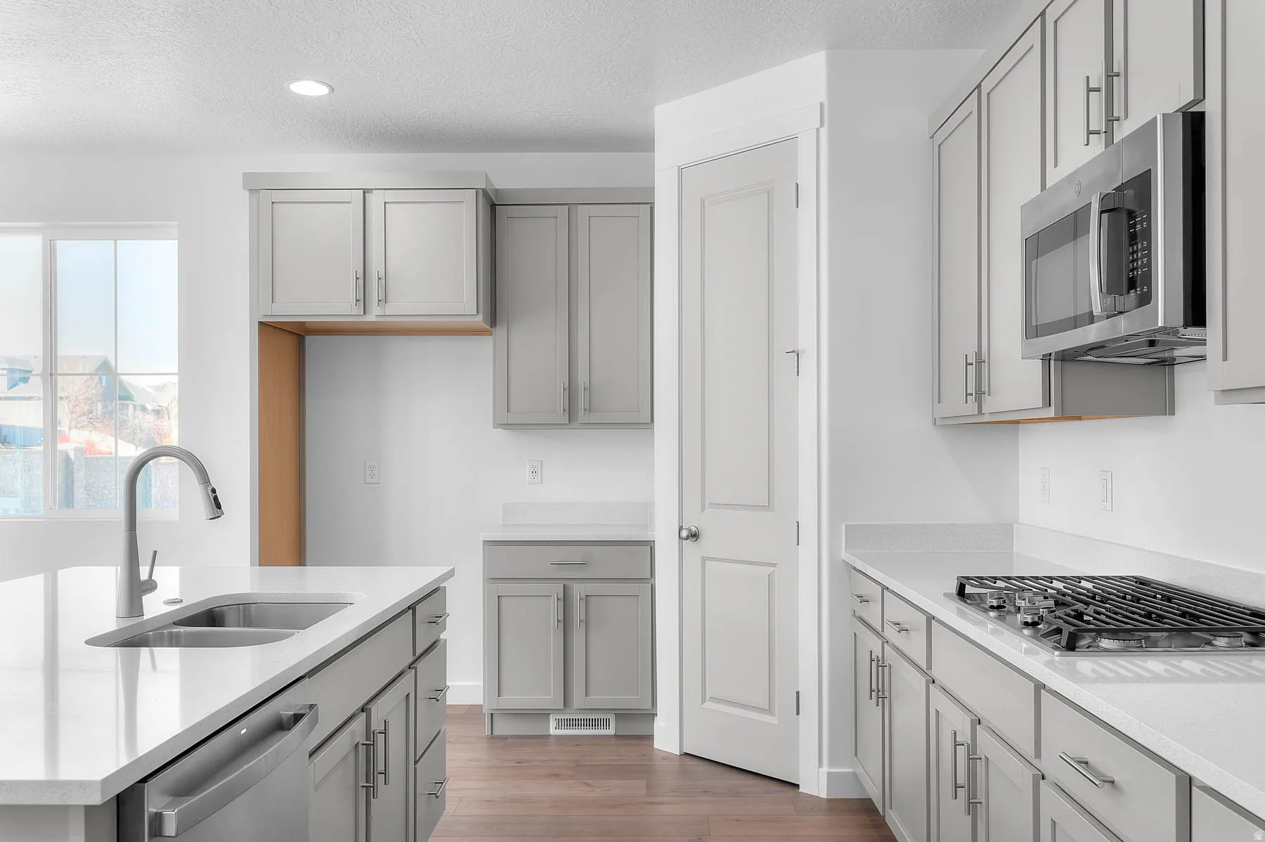 Kitchen featuring light gray cabinetry, white countertops, stainless steel appliances, and wood-finish flooring