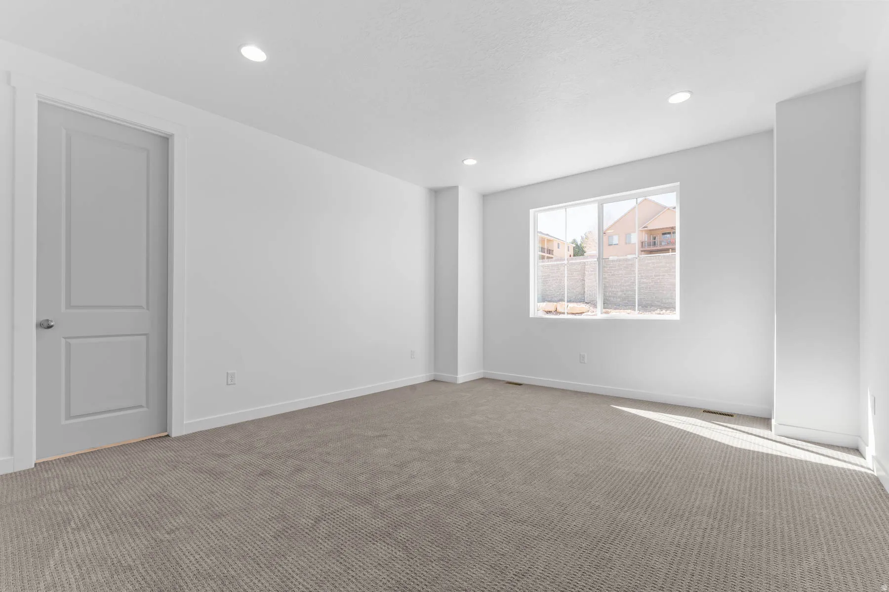 Recessed lighting, light gray two-panel interior door, plush carpet flooring, white walls, and a large window
