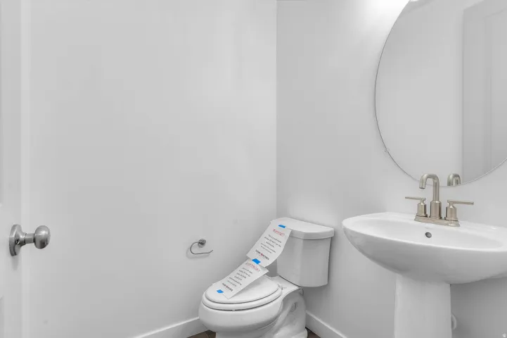 Pedestal sink with a round mirror, brushed nickel faucet, and a toilet