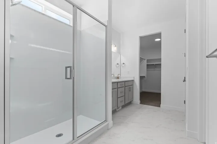 Glass-enclosed shower with a transom window, dual vanity with undermount sinks, gray cabinetry, and light-toned flooring
