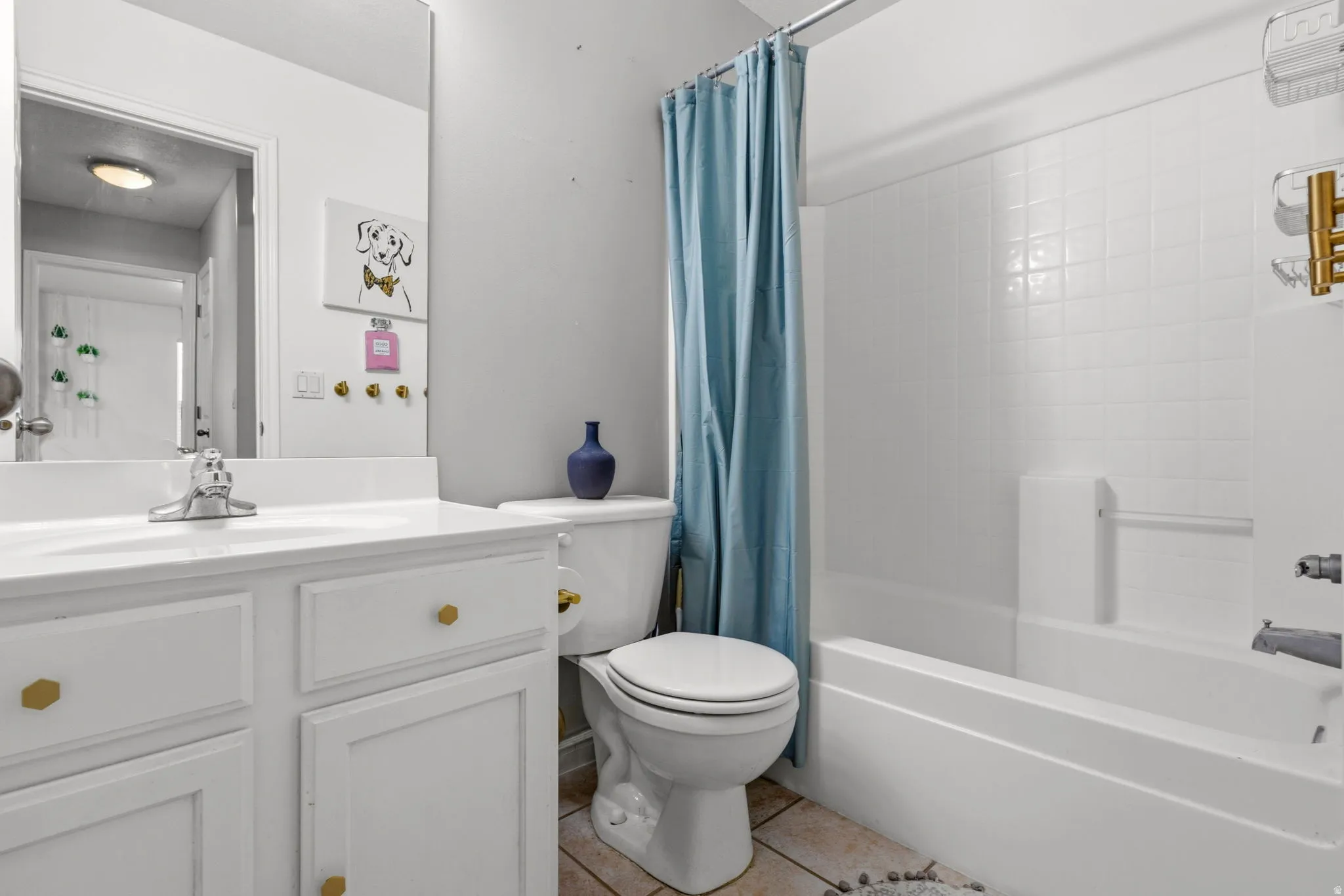 White vanity with hexagon gold-tone hardware, full-width mirror, white toilet, and white tub/shower combination with tiled surround