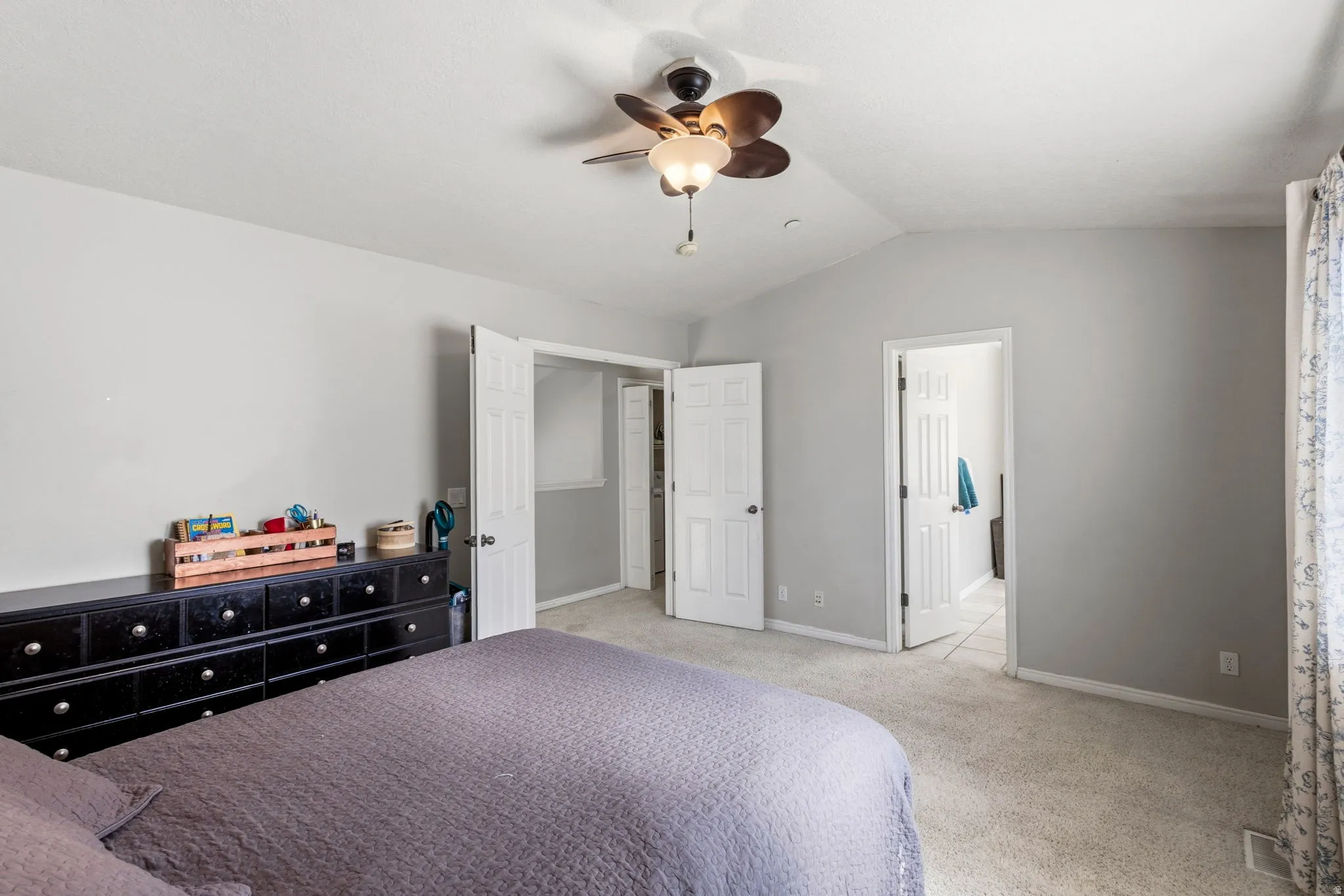 Vaulted ceiling, ceiling fan with light fixture, light gray wall paint, carpet flooring, multiple interior doors