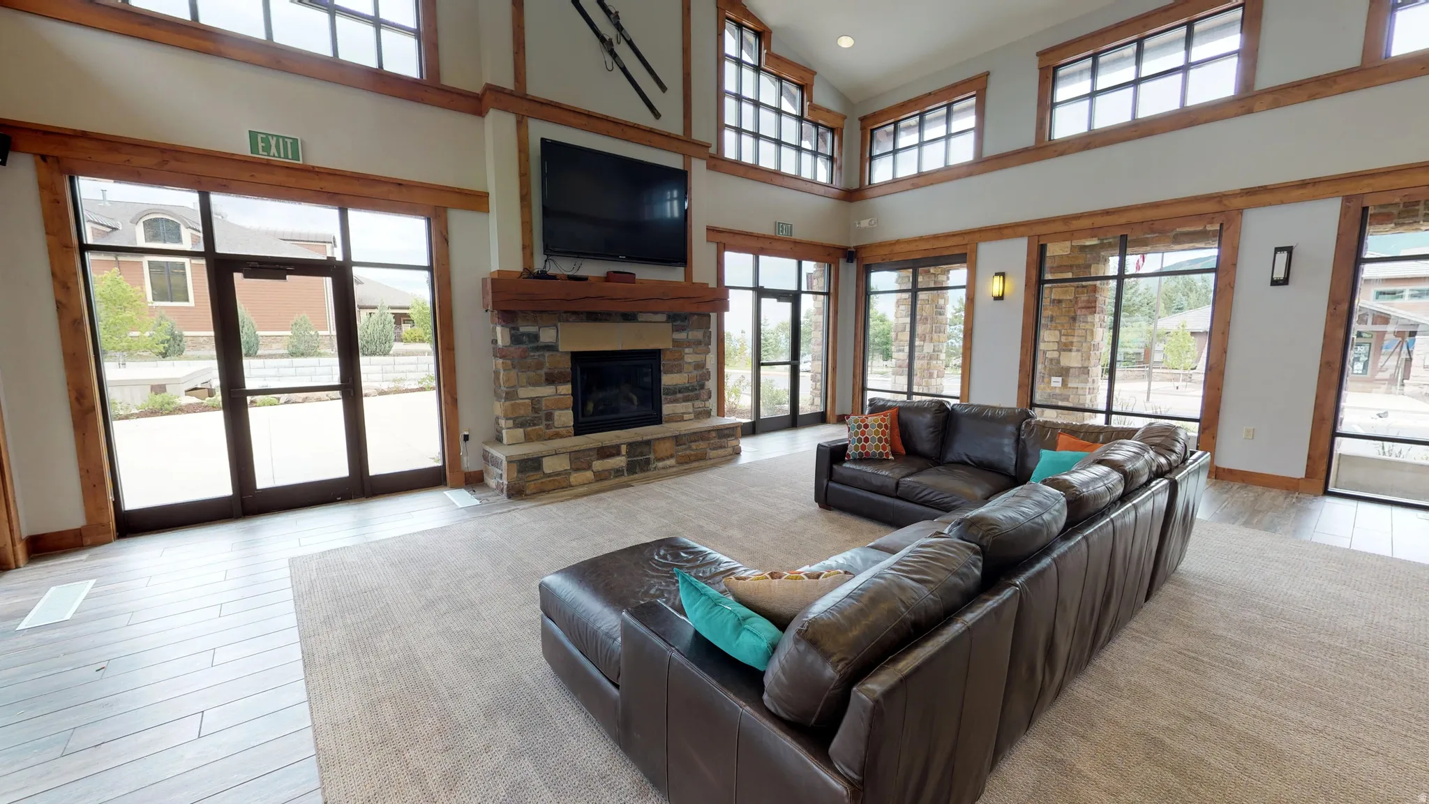 Vaulted ceilings, a stone-clad fireplace, large windows with dark frames, exposed wood beams, and a blend of carpet and wood-finish flooring
