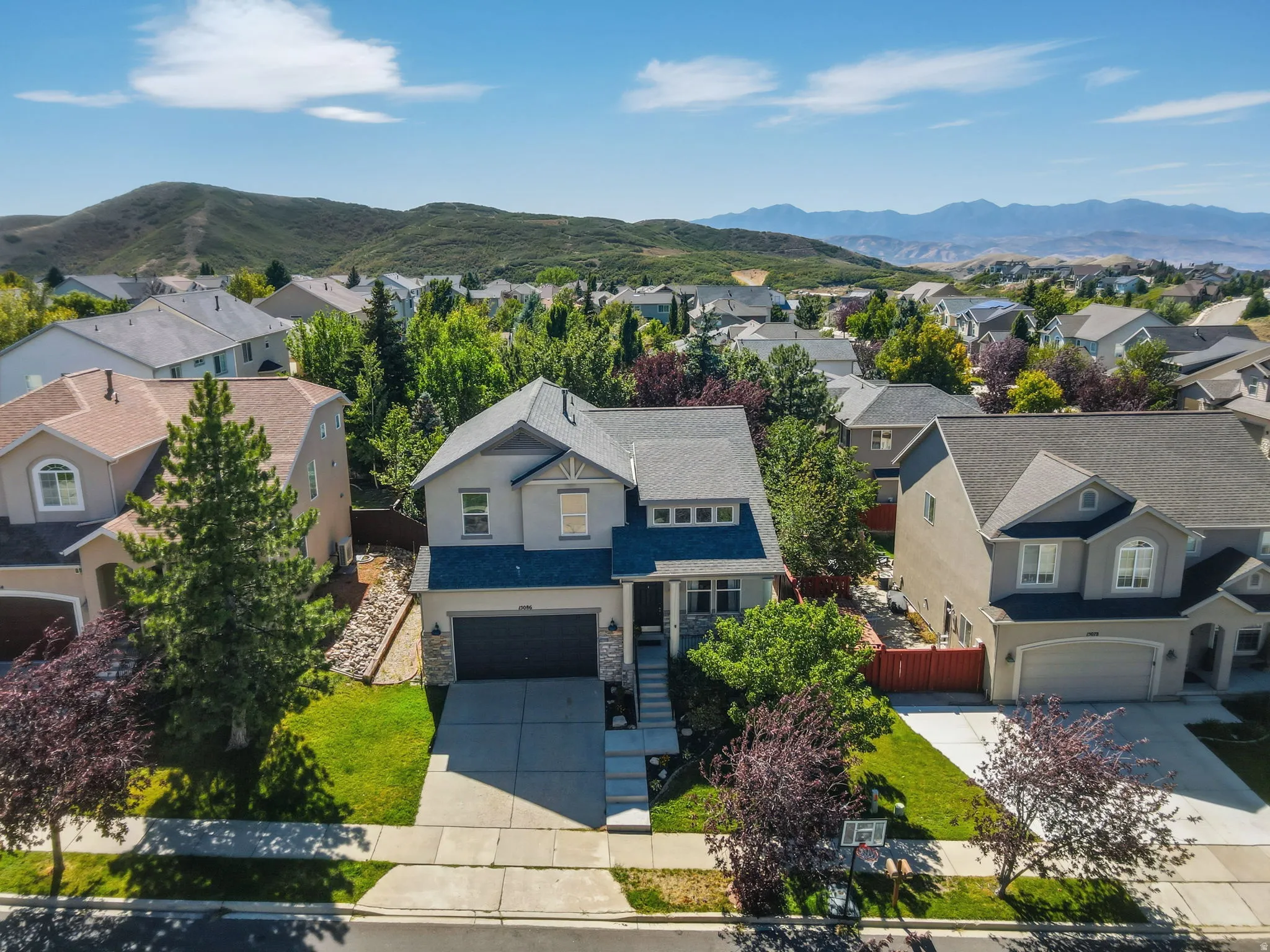 Two-story stucco exterior with stone accents, attached two-car garage, mature landscaping, and a concrete driveway
