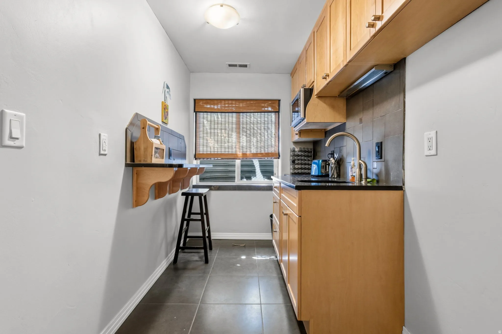 Compact kitchen with wood-finish cabinetry, dark countertop, and tile flooring