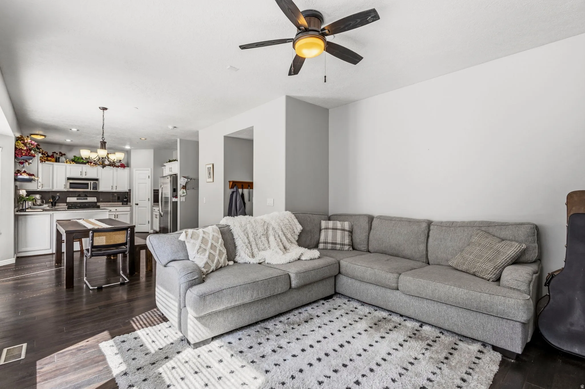Open-concept living space featuring wood-finish flooring, a ceiling fan with integrated lighting, and a kitchen with white cabinetry and stainless steel appliances