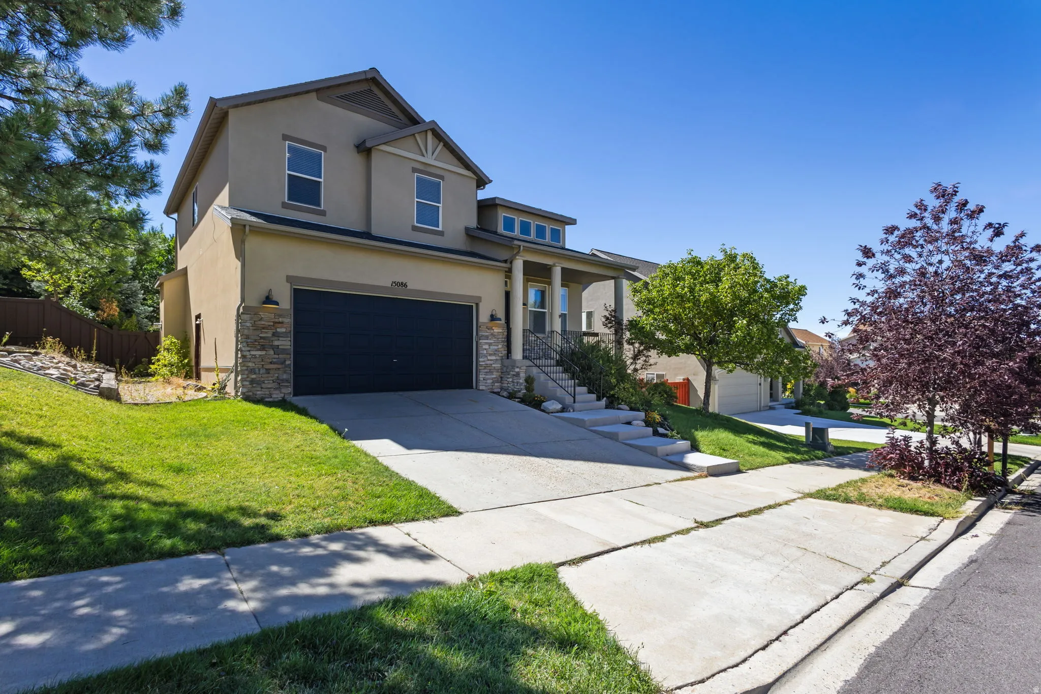 Stucco and stone exterior, two-car garage, concrete driveway, covered porch, and mature landscaping