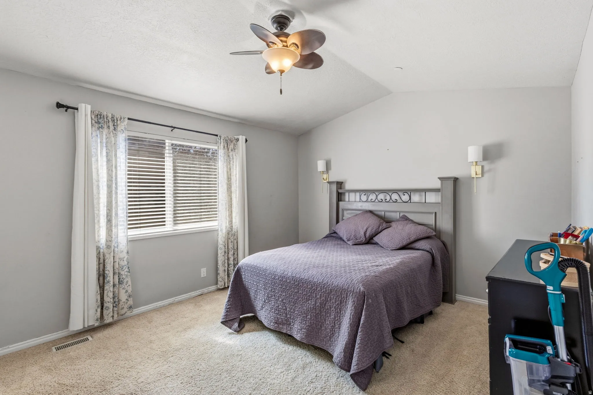 Vaulted ceiling with a ceiling fan, window with blinds, wall-mounted sconces, and neutral-toned carpeting
