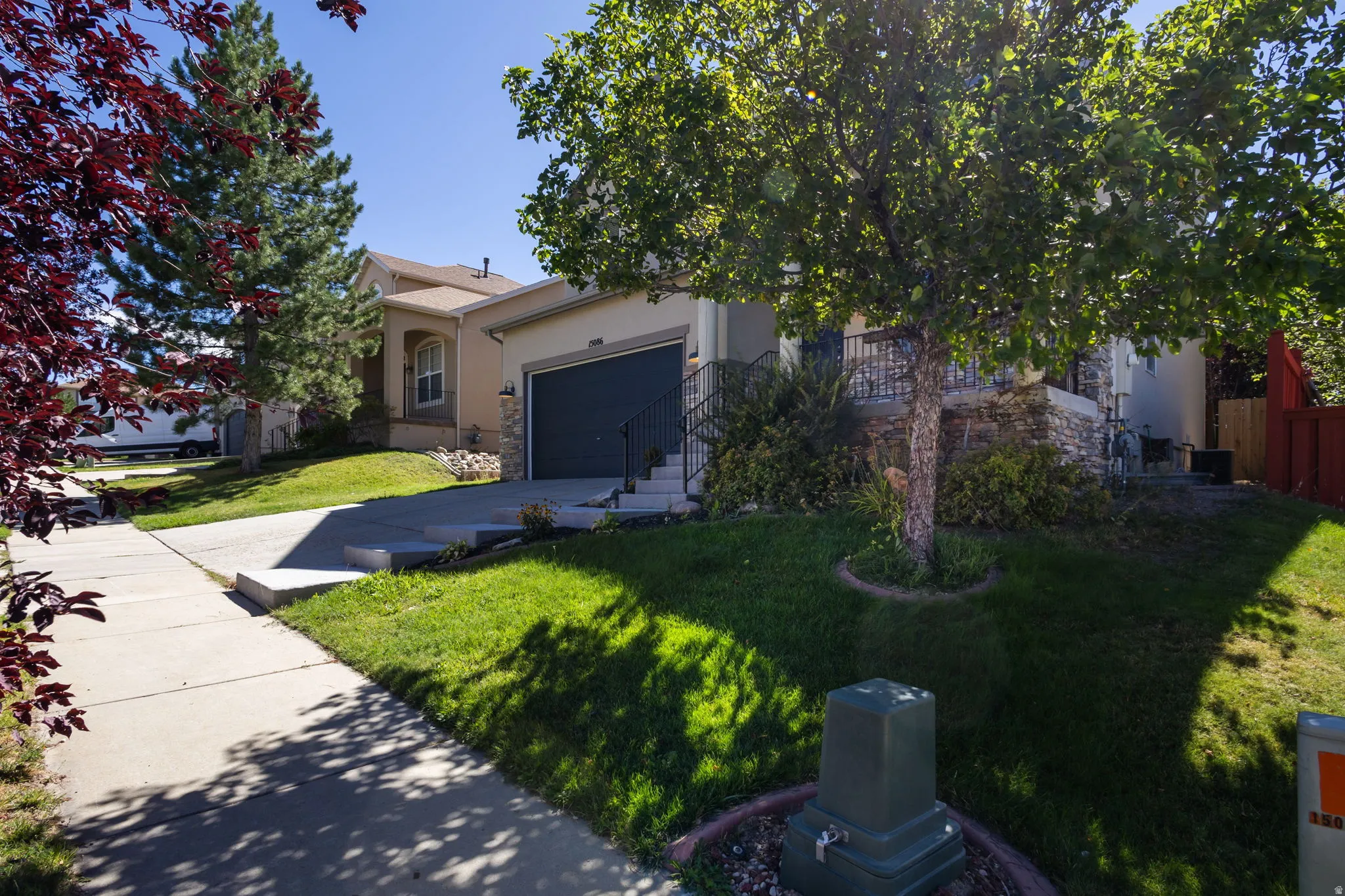 Exterior featuring stucco siding, stone facade accents, an attached garage, a concrete driveway, and a front porch with black iron railing