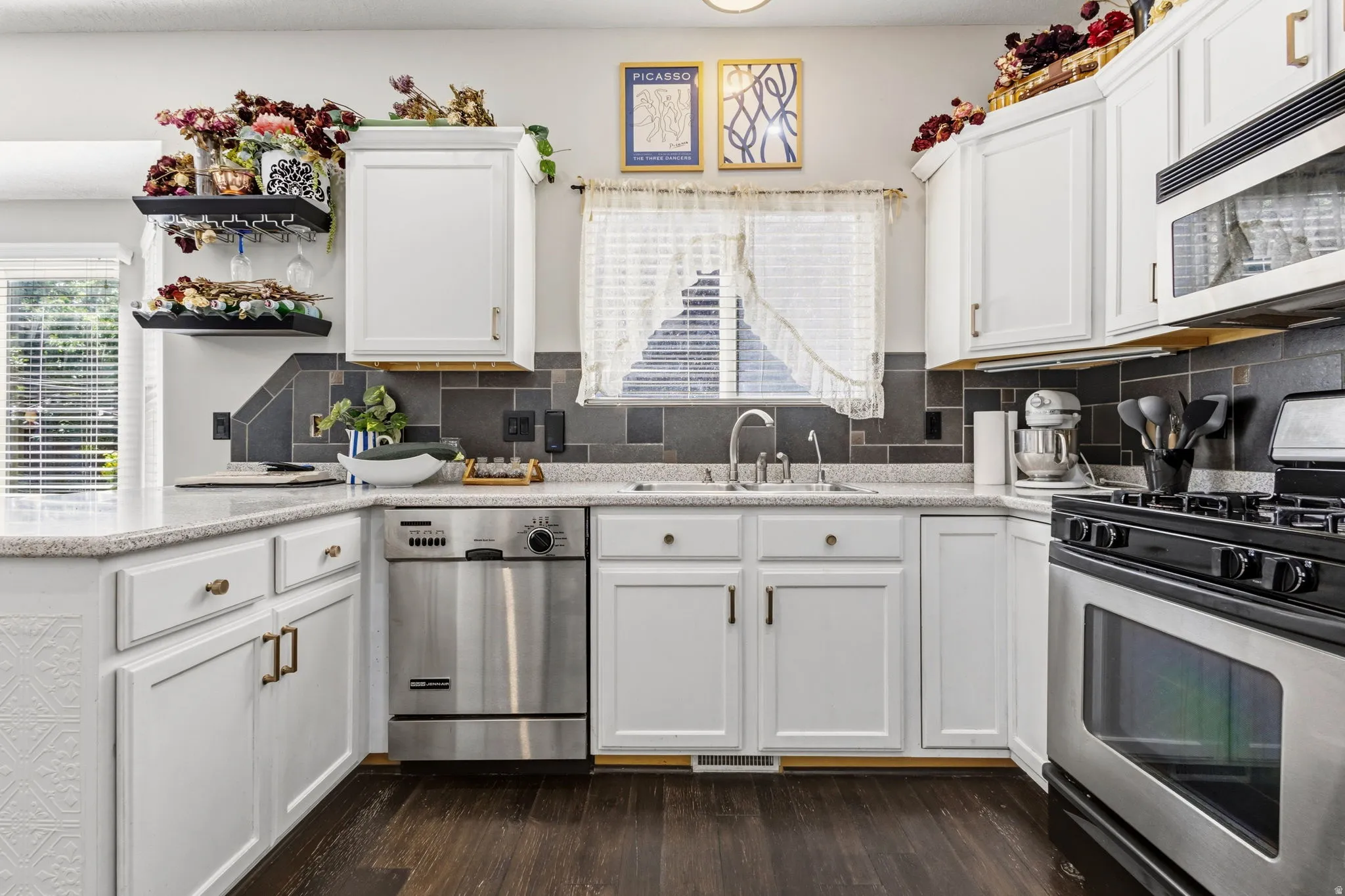 White cabinetry, stainless steel appliances, dark tile backsplash, light-toned countertops, and dark wood-finish flooring