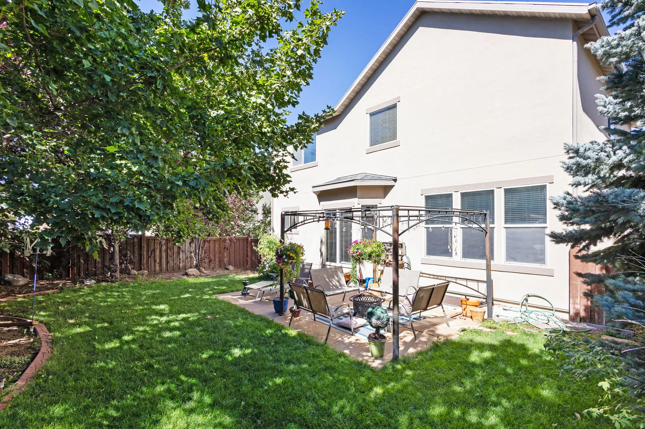 Rear stucco exterior with multiple windows, a concrete patio, and a metal gazebo frame