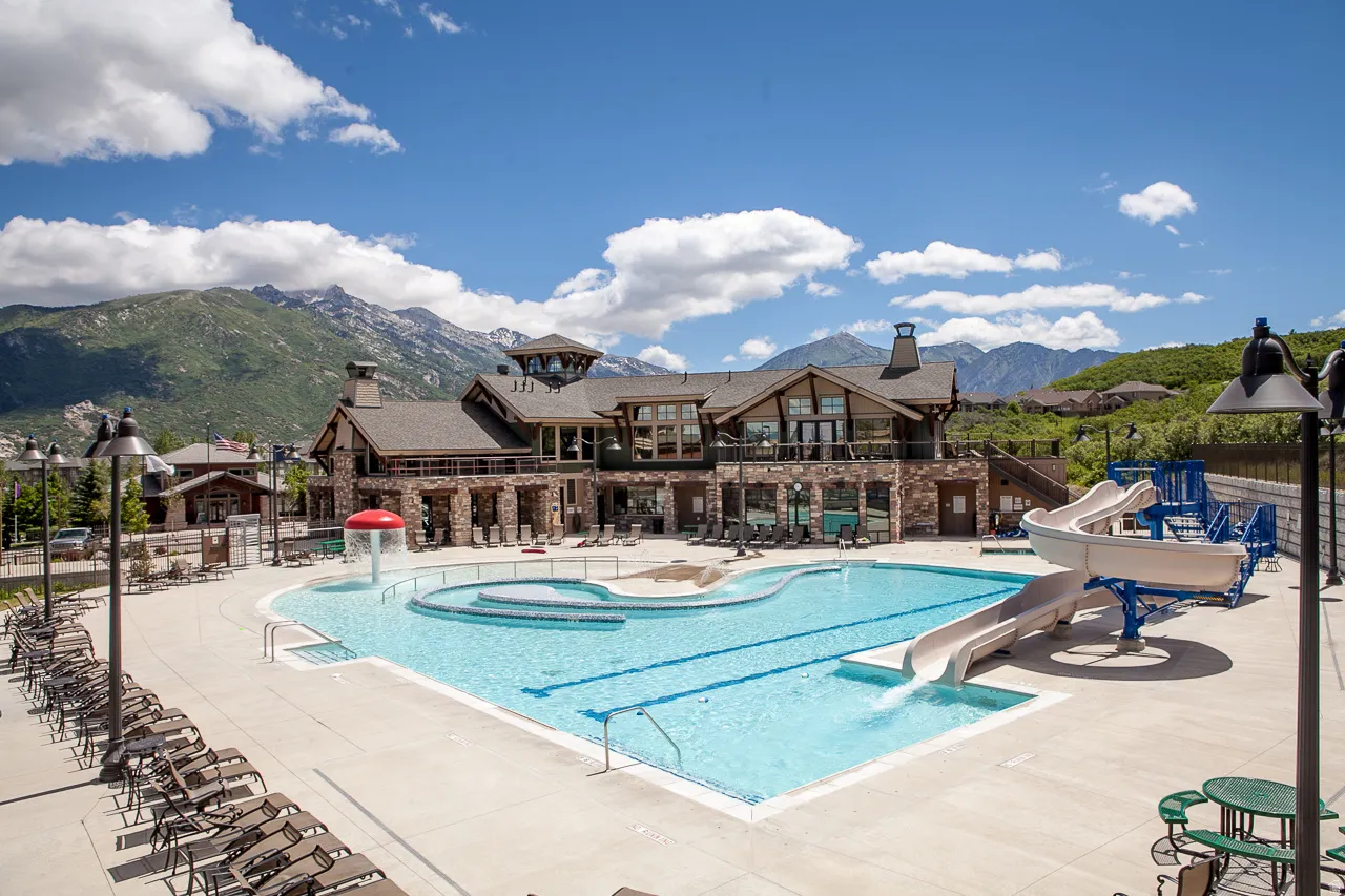 Resort-style pool with integrated water slide and sun shelf, bordered by extensive concrete decking