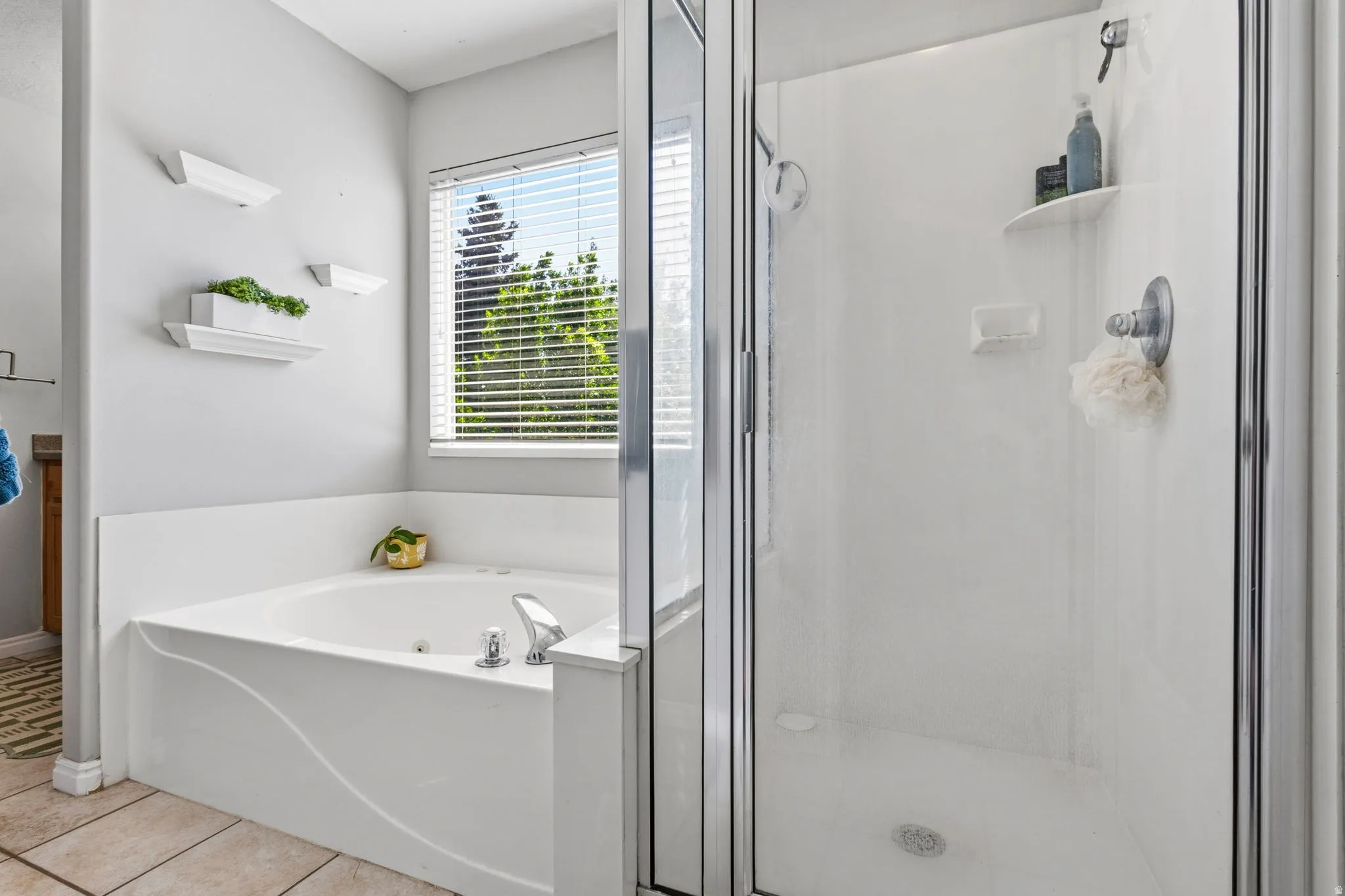 Jetted soaking tub, walk-in shower with glass enclosure, chrome fixtures, and window with blinds