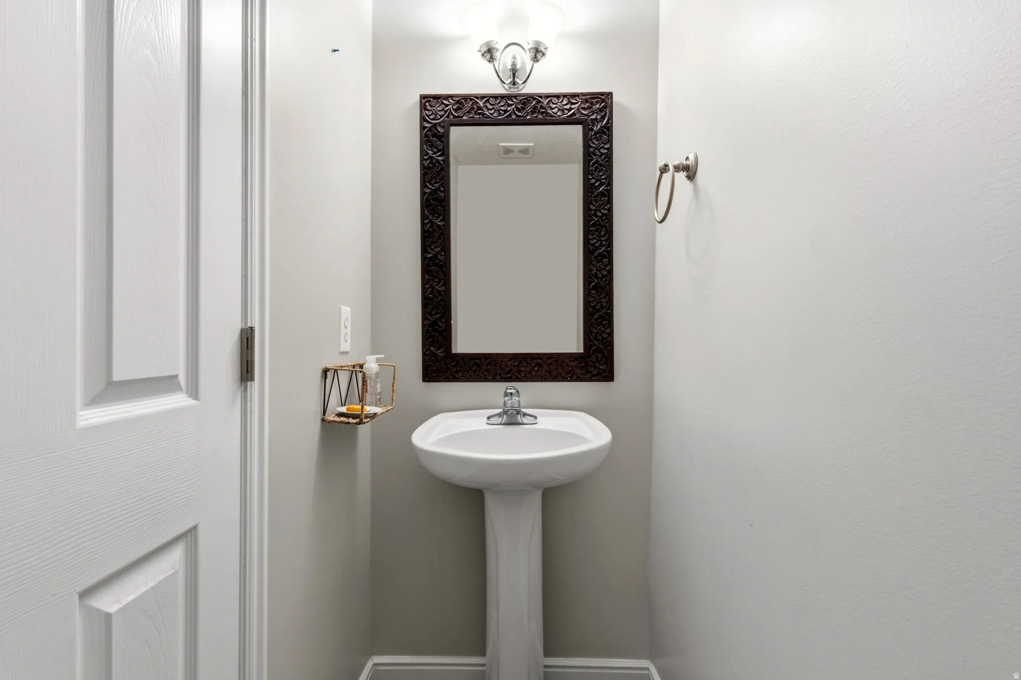 Pedestal sink with chrome faucet, framed mirror, and wall-mounted light fixture