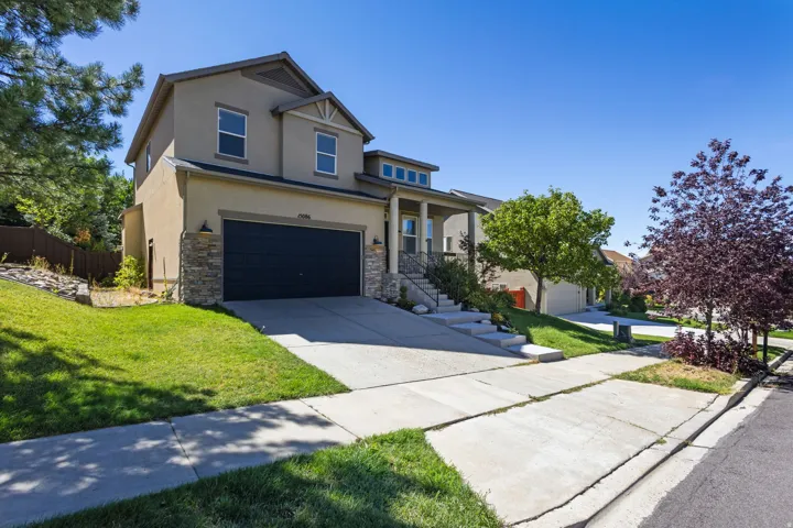 Stucco and stone exterior, two-car garage, concrete driveway, covered porch, and mature landscaping