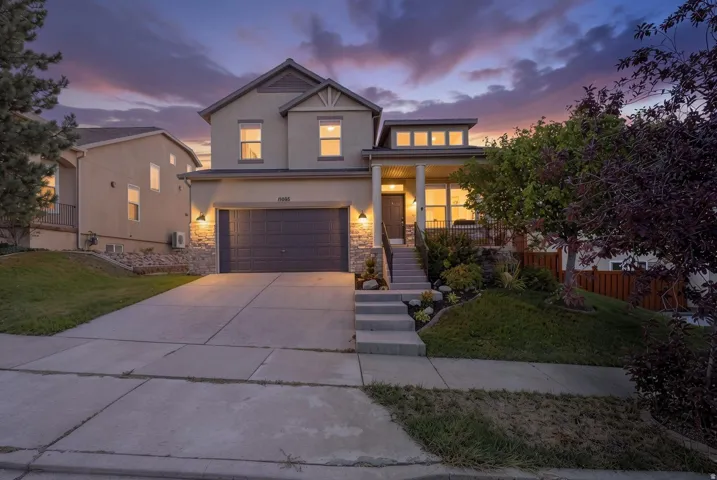 Two-story stucco exterior with stone accents, featuring a multi-pane garage door, covered porch with columns, and concrete driveway