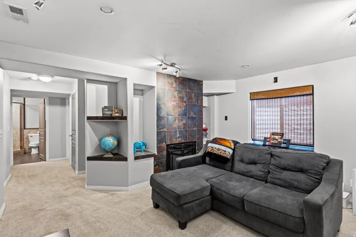 Recessed lighting, track lighting, built-in shelving, carpet flooring, and a window with a woven shade