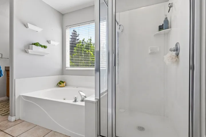 Jetted soaking tub, walk-in shower with glass enclosure, chrome fixtures, and window with blinds
