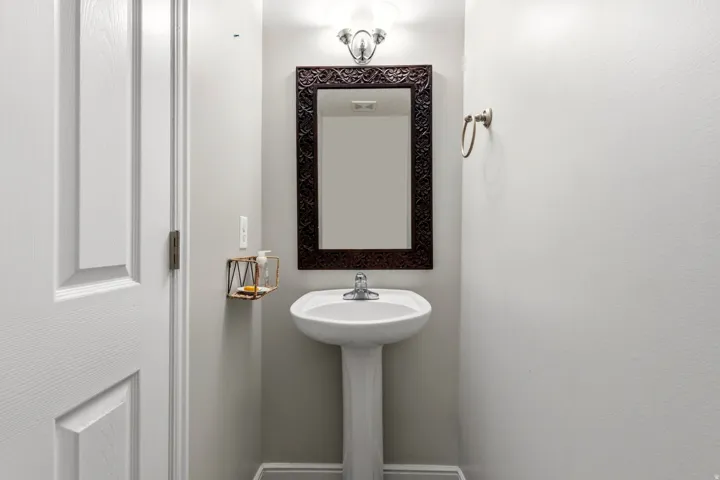 Pedestal sink with chrome faucet, framed mirror, and wall-mounted light fixture