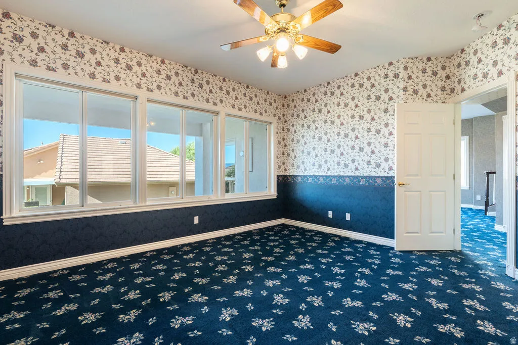 Wall-to-wall carpeting with a floral pattern, multiple windows providing natural light, a ceiling fan with integrated lighting, and a white paneled door