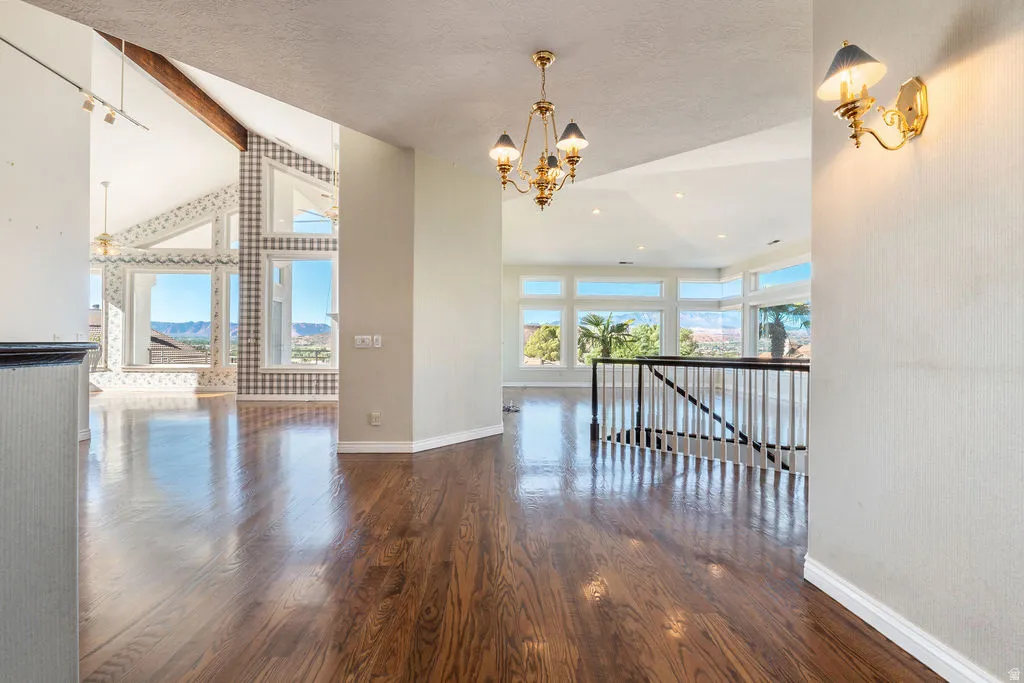 Vaulted ceilings with exposed wood beams, expansive windows, wood-finish flooring, and a decorative chandelier