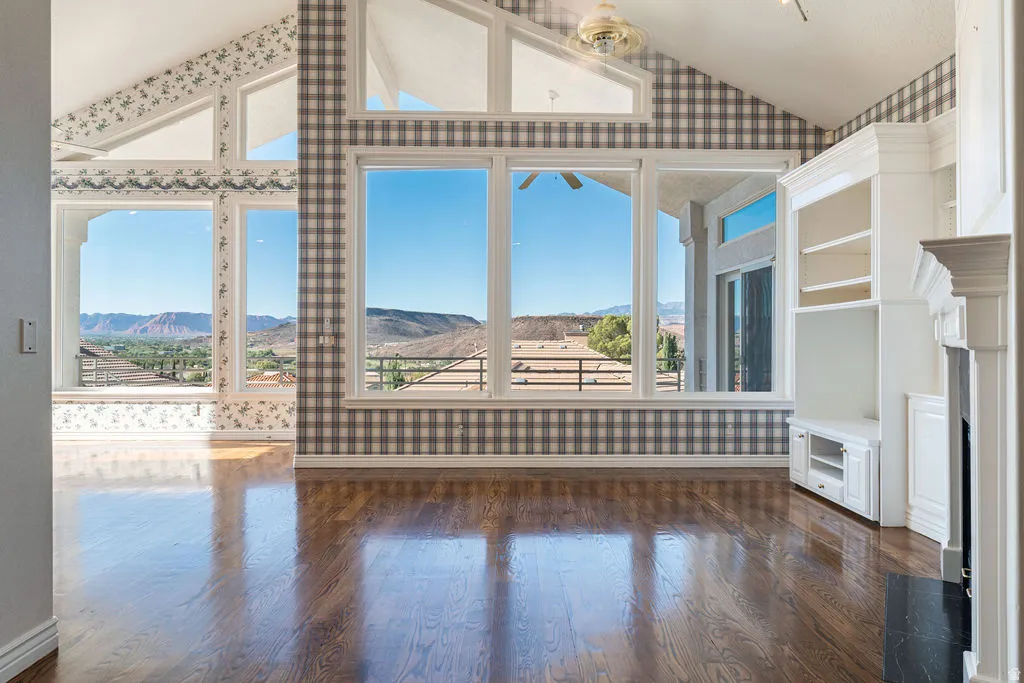 Vaulted ceilings, expansive windows, wood-finish flooring, built-in cabinetry, and a prominent fireplace with a black surround