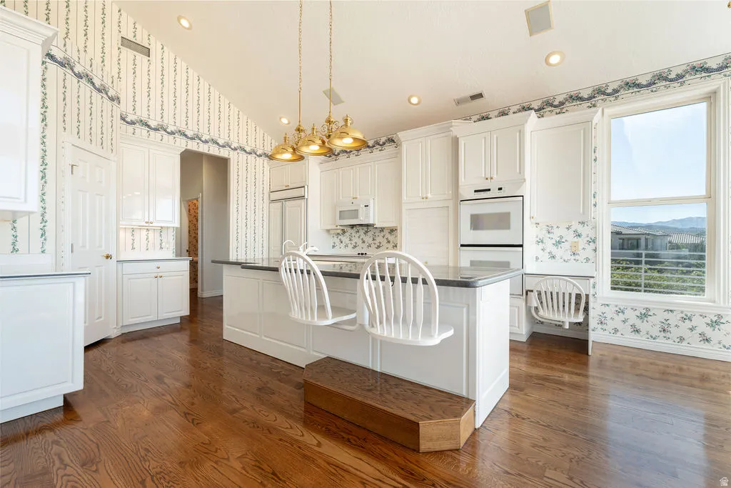 Kitchen featuring wood-finish flooring, white cabinetry, a built-in double oven, recessed lighting, and a window with distant scenery