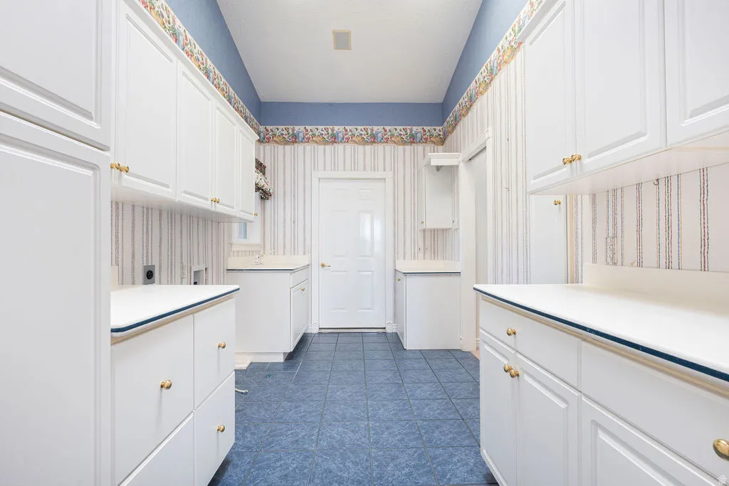 White cabinetry with gold-tone hardware, white countertops, tiled flooring, and a white door