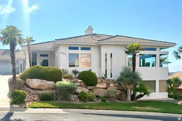 Stucco exterior with a tiled roof, multi-level landscaping featuring rock work and mature plantings, and integrated garage