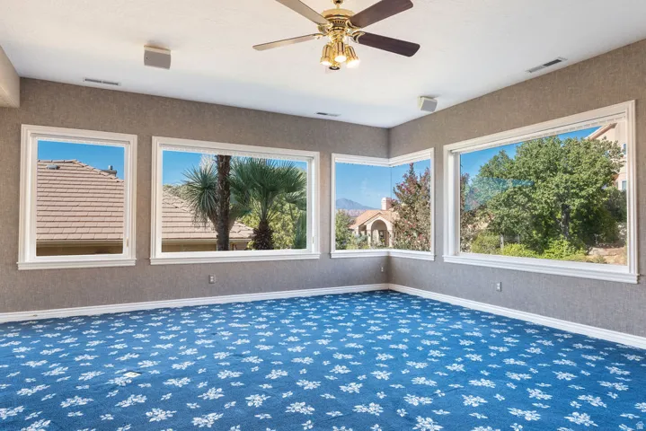 Room featuring multiple large windows, textured wall coverings, and a ceiling fan with integrated lighting