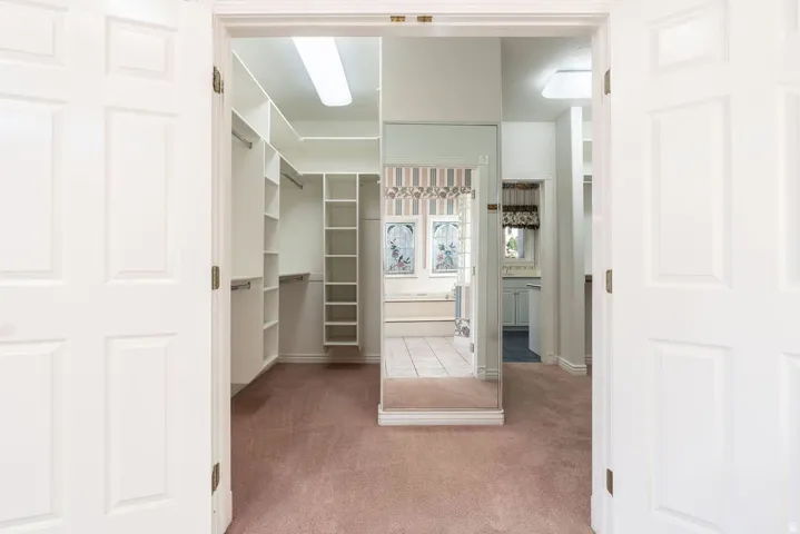 White paneled double doors open to a carpeted dressing room with built-in shelving, hanging rods, and a full-length mirror