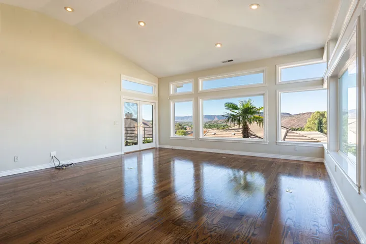 Vaulted ceiling, recessed lighting, expansive windows, glass French doors, and wood-finish flooring