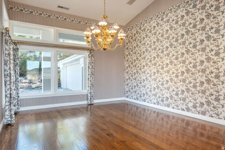 Vaulted ceiling with an ornate brass chandelier, wood-finish flooring, and large windows with transom panels