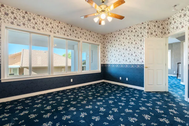 Wall-to-wall carpeting with a floral pattern, multiple windows providing natural light, a ceiling fan with integrated lighting, and a white paneled door
