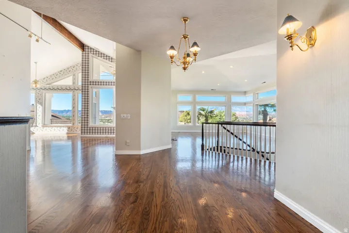 Vaulted ceilings with exposed wood beams, expansive windows, wood-finish flooring, and a decorative chandelier