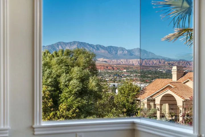 Window with decorative trim framing distant mountains, a city panorama, and a tiled roof structure