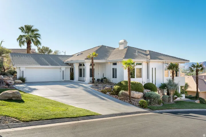 Stucco exterior with a tiled roof, attached two-car garage, concrete driveway, and established landscaping