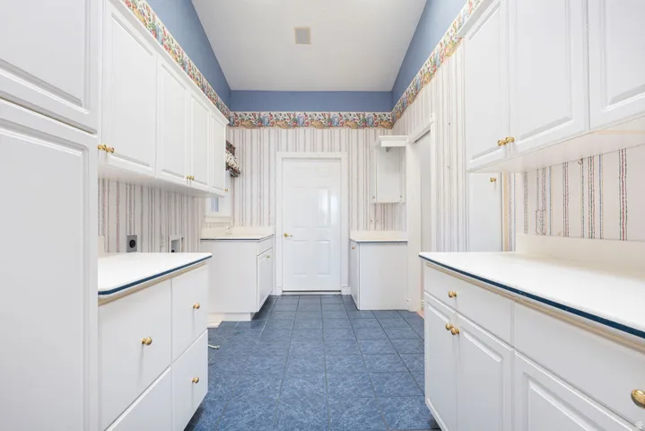 White cabinetry with gold-tone hardware, white countertops, tiled flooring, and a white door