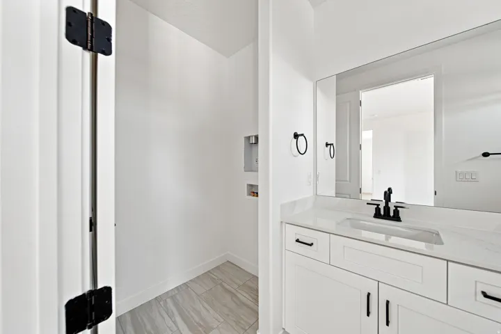 White vanity with black hardware, integrated sink, and a large wall-mounted mirror and washer/dryer hookups